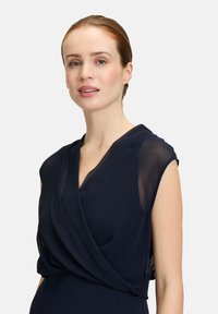 Robe bleu marine avec un design portefeuille, des manches courtes transparentes et une texture lisse ; silhouette élégante avec taille ajustée.