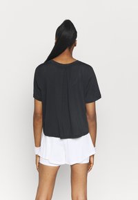 Camiseta negra recortada con mangas cortas, ajuste holgado y una textura sutil, combinada con pantalones cortos deportivos blancos. Sin logotipos ni patrones visibles.