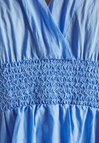 Vestido azul claro con cuerpo fruncido, tejido suave y textura, y falda acampanada que resalta los detalles plisados.