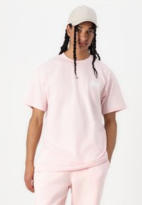 Rosa Baumwoll-T-Shirt mit kurzen Ärmeln und Rundhalsausschnitt, mit einem kontrastierenden Logo-Detail auf der Brust. Kombiniert mit passenden Jogginghosen.
