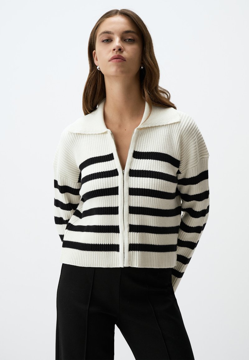 Cardigan a maglia con texture a costine, caratterizzato da strisce orizzontali alternate nere e bianche, colletto e chiusura centrale con zip.