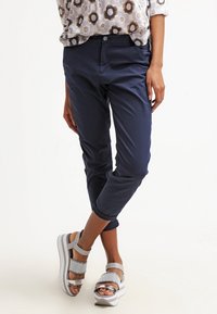 Marinblå cropped-byxor med en slät textur, parat med silverfärgade sandaler med en perforerad rem och tjock vit sula.