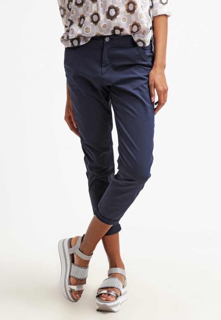 Marinblå cropped-byxor med en slät textur, parat med silverfärgade sandaler med en perforerad rem och tjock vit sula.