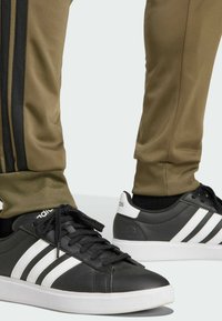 Svarta sportskor med tre vita ränder på sidan, matchade med olivgröna avsmalnande byxor med svarta sidostripes.