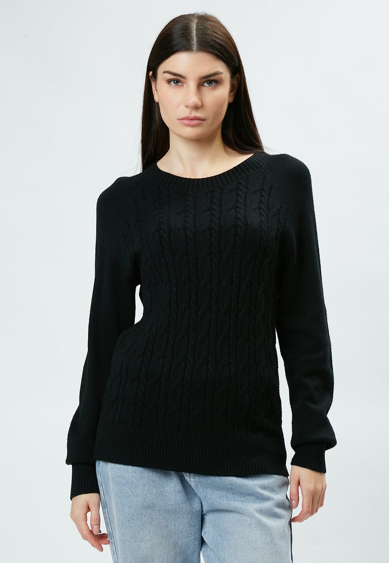 Pull en tricot noir avec une texture en torsades, des poignets et un ourlet rayés, et un col rond. Associé à un jean bleu clair.