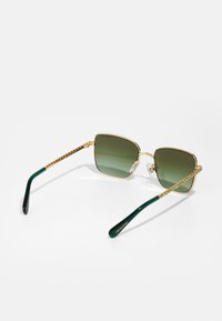 Kvadrātveida zaļas saulesbrilles ar zeltītām metāla rāmēm, zaļiem akcentiem uz kājām un kristāla detaļām gar kājām.