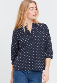 Blusa blu navy con scollo a V, maniche a tre quarti, con motivi floreali bianchi e righe verticali. Tessuto morbido con vestibilità rilassata.