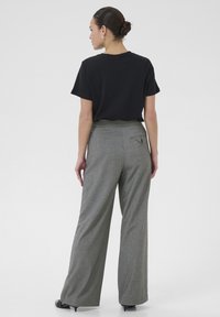 Pantalones de pierna ancha en un patrón de espiga gris con una cintura alta y bolsillos laterales, combinados con una camiseta negra de corte holgado.