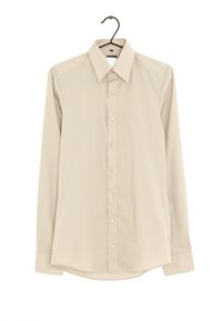 Chemise à manches longues beige clair sur un cintre, avec un col pointu, une fermeture à boutons à l'avant et un tissu lisse légèrement texturé.