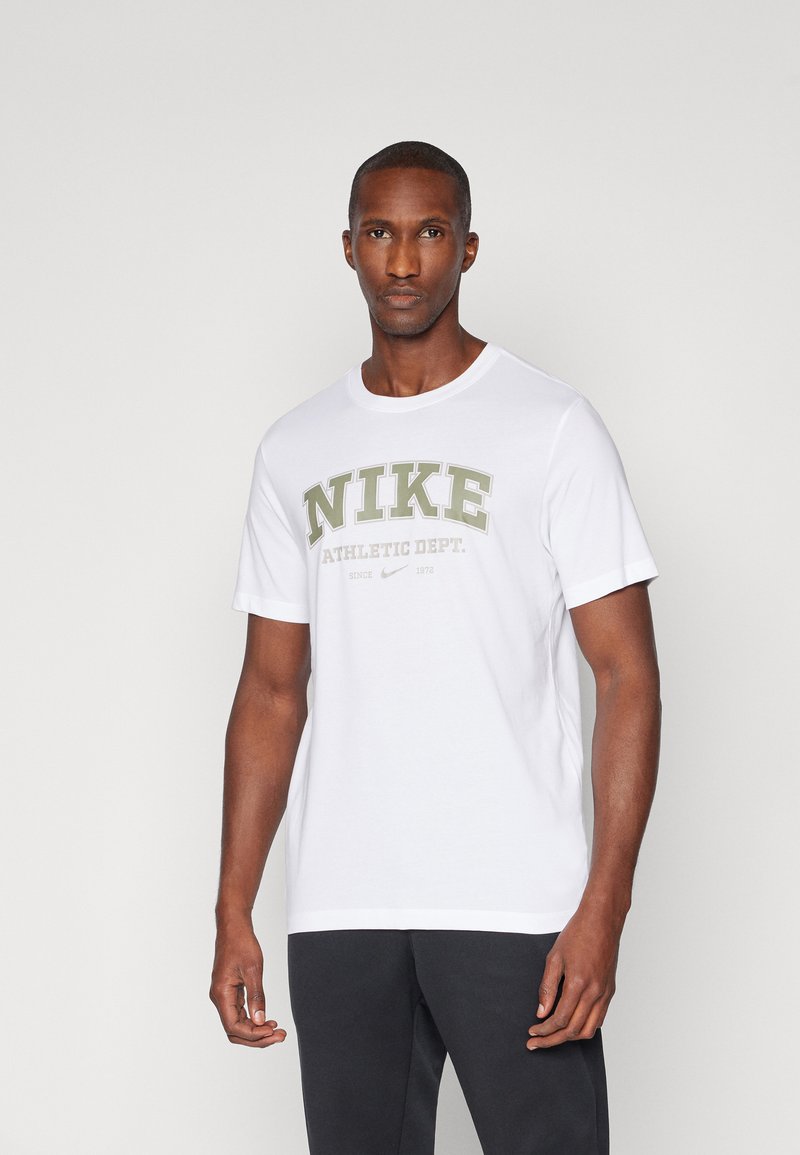 T-shirt bianco in cotone con grande scritta verde "NIKE" e "ATHLETIC DEPT." grigio sottostante. Semplice scollatura rotonda e maniche corte.