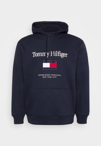 Tengerészkék kapucnis pulóver pamutkeverékből készült. Elöl zsebe van, húzózsinóros kapucnival és hímzett logóval rendelkezik, amely téglalap alakú, háromszínű mintával díszített.