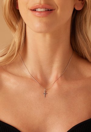 Halskette aus Sterlingsilber mit feiner Kette und kleinem Kreuzanhänger, der auf einem nackten Hals mit glatter Hautstruktur ruht.
