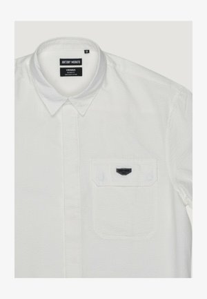 Camicia bianca a maniche corte con texture, bottoni frontali, colletto appuntito e taschino sul petto con l'etichetta "Antony Morato Vienna".