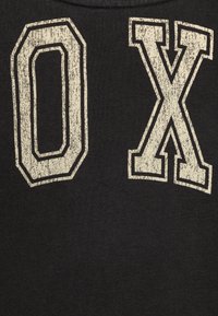 Čierna látka s opotrebovanými bielymi potlačenými písmenami "0" a "X" v tučnom type písma, s textúrovaným povrchom a mierne opotrebovaným vzhľadom.
