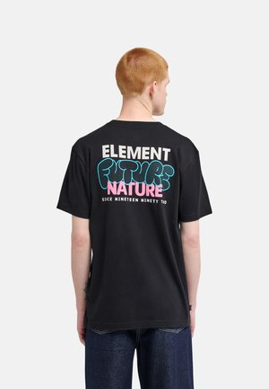 Jeune personne aux cheveux rouges courts portant un T-shirt noir avec un texte coloré "ELEMENT FUTURE NATURE SINCE NINETEEN NINETY TWO" dans le dos.