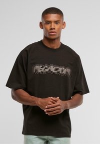 Sort oversized T-shirt lavet af bomuld med et stort, stiliseret gråt logo hen over brystet. Korte ærmer og rund halsudskæring.