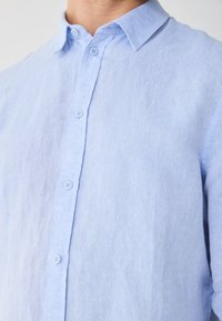 Light blue linen shirt with a button-down collar, front button closure, and subtle texture. Short sleeves are visible at the edges.
