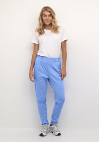 Lichtblauwe, taps toelopende broek met een gladde textuur en zijzakken, gecombineerd met een effen wit T-shirt en grijze sneakers.