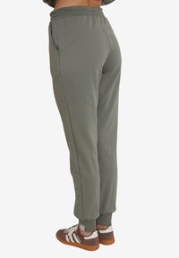 Oliwkowe dresy o zwężanym kroju, z elastycznym paskiem w talii, bocznymi kieszeniami i ściągaczami na nogawkach, wykonane z miękkiego, elastycznego materiału.