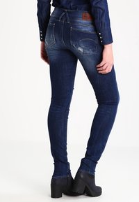 Jeans ajustados azul oscuro con una textura desgastada, que presentan una cintura alta y bolsillos traseros, combinados con botines negros de tacón.