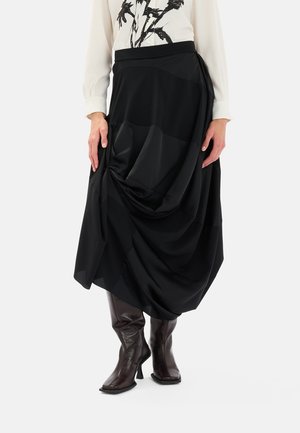 Gonna nera midi con design drappeggiato, caratterizzata da una texture liscia e sezioni plissettate. Abbinata a stivali marroni scuri al ginocchio.