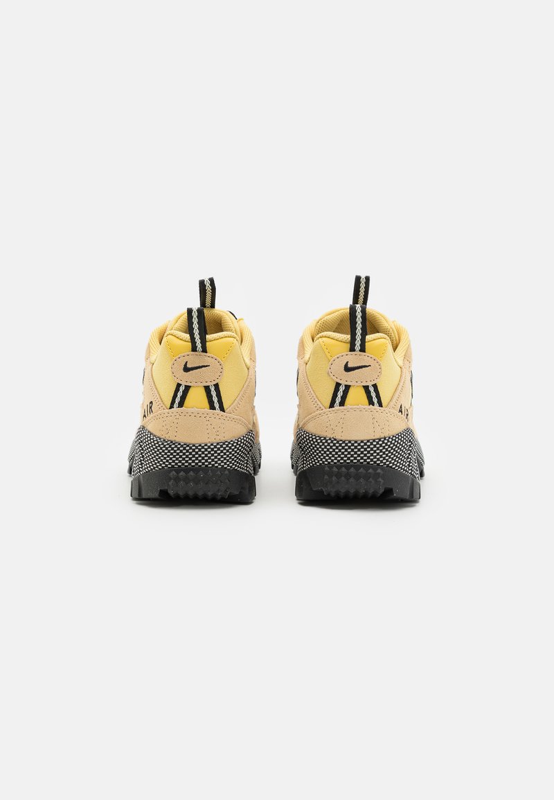 Baskets Nike avec un dessus jaune et beige, semelle noire et accents texturés, comprenant une languette de traction et un logo au niveau du talon.