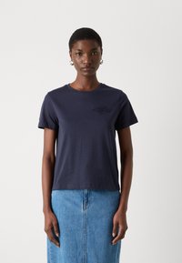 Námornícky modré bavlnené tričko s krátkymi rukávmi, okrúhlym výstrihom a jemne vyšitým dizajnom na hrudi. Skombinované s džínsovou sukňou.