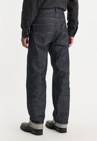 Mörkblå denimjeans med synlig sömnad, rak benmodell och bakfickor. Bärs med svarta stövlar och uppvikta benslut.