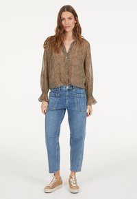 Brown animal print blouse with button-down front, loose sleeves. Worn with blue cargo-style jeans, featuring multiple pockets, and beige sneakers.