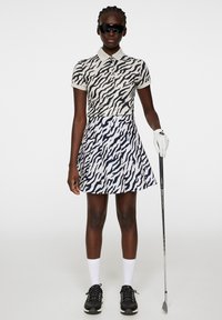 Set polo e gonna in stampa zebrate bianco e nero, con colletto, tessuti testurizzati e un design di gonna a pieghe. Accessorio per il golf di colore nero.