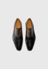 Chaussures en cuir noires avec une finition lisse, présentant une partie supérieure texturée marron, un bout pointu et six trous pour les lacets.