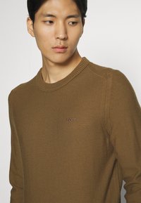 Brauner Strickpullover mit geripptem Rundhalsausschnitt und gesticktem "BOSS"-Logo auf der Brust. Glatte Textur mit schmal zulaufender Armform.