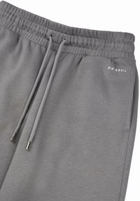 Pelēkas sporta bikses ar elastīgu jostu, saites slēgšanu un sānu kabatām. Uz tām ir mazs balts "OH APRIL" logotips. Mīksta, teksturēta auduma.