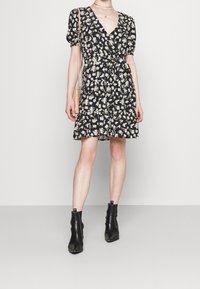 Robe florale noire à manches bouffantes, décolleté en V, taille cintrée et jupe à volants. Portée avec des bottines noires et un petit sac bandoulière rose.