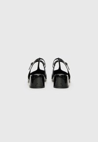 Black patent leather heels with a block heel, open back design, and adjustable strap; smooth surface with minimal accents.