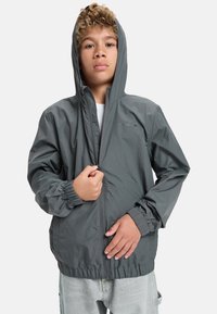 Grå vindjacka med huva, elastiska ärmslut och justerbar nederkant. Dragkedja fram och logotypdetalj på bröstet. Lätt och slät textur.