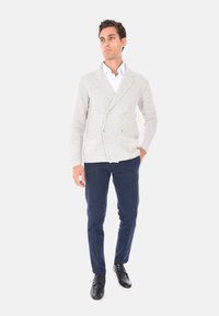 Cardigan doppiopetto grigio chiaro con bottoni dorati, abbinato a pantaloni blu scuro e scarpe nere. Tessuto liscio con una vestibilità comoda.