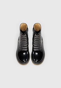Bottes de cheville en cuir patent noir avec un bout arrondi, des lacets argentés et une fermeture éclair sur le côté. Semelle texturée marron avec des détails de surcoutures blanches.