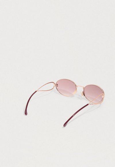 Gafas de sol redondas de tono rosa con montura de metal color oro rosa y puntas de las patillas en marrón, reposan sobre una superficie clara.