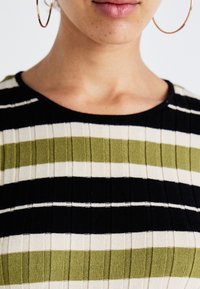 Gestreepte gebreide top met afwisselende banden van olijfgroen, wit en zwart, voorzien van een geribbelde textuur en een ronde halslijn.