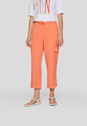 Pfirsichfarbene Cargo-Hosen bis zur Mitte der Waden mit einem elastischen Bund, Seitentaschen und einem leichten Stoff. Kombiniert mit beigen Sandalen.