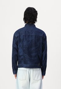 Jeansjacka i mörkblått med texturerade mönster, krage och knappade manschetter, i kombination med ljusblå jeans.