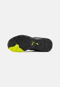 Scarpa sportiva con suola in gomma nera con accenti gialli, motivo di battistrada texture e tallone rinforzato per stabilità.