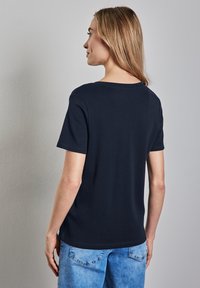 Námořnická modrá tričko s krátkým rukávem a kulatým výstřihem, vyrobené z měkké bavlněné tkaniny. Nabízí volný střih a jemné detaily v prošívání.