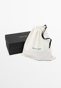 Boîte rectangulaire noire Massimo Dutti avec pochette blanche à cordon comportant des cordons noirs et le logo Massimo Dutti sur le devant.