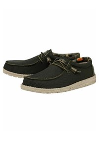 Scarpe slip-on in rete nera con suole beige maculate, accenti verdi e un motivo interno mimetico. Presentano una chiusura con lacci per una vestibilità sicura.