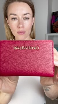 Punane tekstuuriga nahast rahakott kuldse "VALENTINO" logoga. Omab kompaktset ristküliku kujulist vormi ja nähtavaid õmblusi servade ümber.