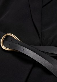 Tissu noir avec une texture lisse, présentant une ceinture en cuir noir ornée d'une boucle ovale en or et de plusieurs trous pour les ajustements.