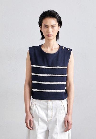 Navy mouwloos top met horizontale witte gestructureerde strepen, schouderknopen en een ronde halslijn, gecombineerd met witte broek.