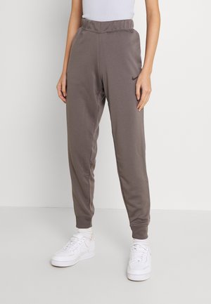 Persoon draagt grijze Nike joggingbroek met omgeslagen enkels en witte sneakers tegen een effen witte achtergrond.
